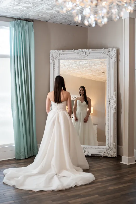 Sarah adjusts her flowing veil in an ornate white-framed mirror before her ceremony at The White Room.