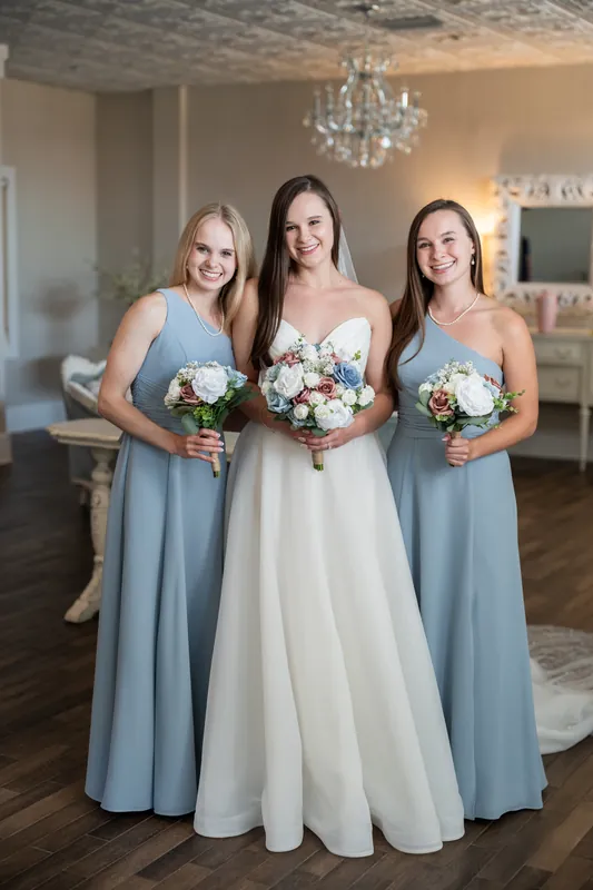 Sarah poses with two bridesmaids holding matching white and blush bouquets in the bridal suite.