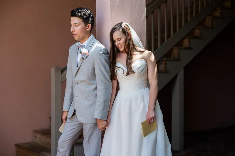 Sarah and Nathan walk down interior stairs together, she in her white gown and he in his gray suit.