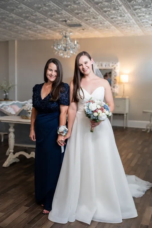 Sarah holds her bouquet next to a bridesmaid in navy, smiling inside The White Room's elegant ballroom.