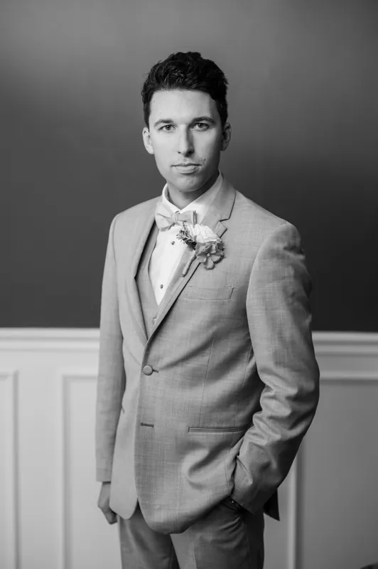 Nathan wears a gray suit with a floral boutonniere, posed against a neutral backdrop in a formal portrait.