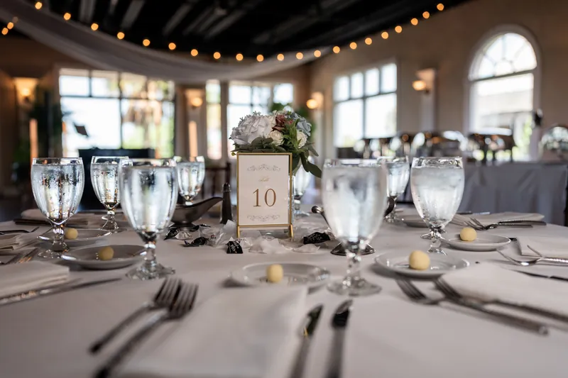 Table 10 centerpiece at The White Room features clear glassware, white linens, and cream candles under string lights.