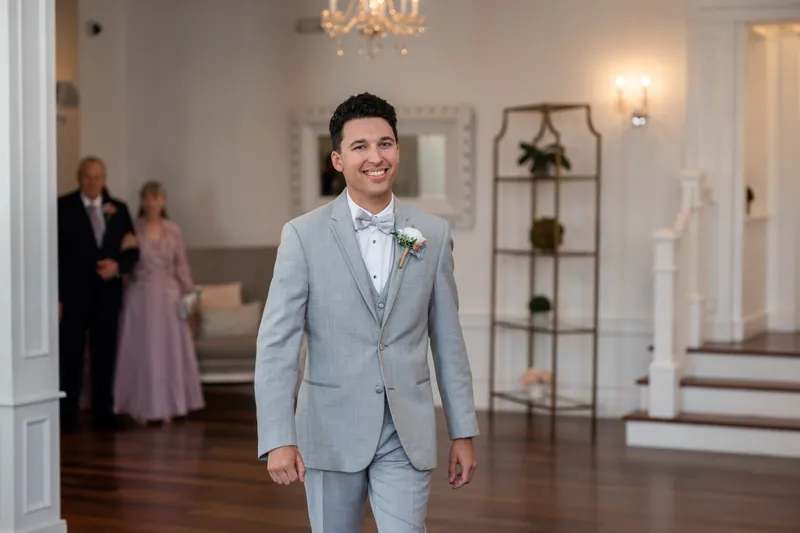 Nathan smiles while walking through The White Room wearing a light blue suit with boutonnière.