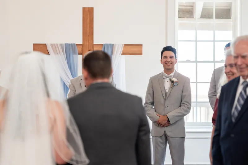 Nathan faces Sarah at the altar beneath a wooden cross, smiling as they prepare to exchange vows at The White Room.