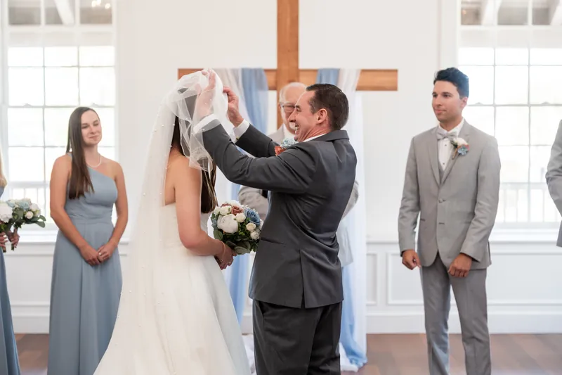 Nathan lifts Sarah's veil at the altar while guests look on during their ceremony at The White Room.