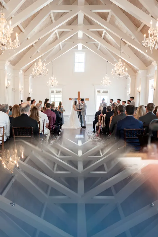 Symmetrical view down the aisle at The White Room showing Sarah and Nathan at the altar, soaring ceiling with exposed beams