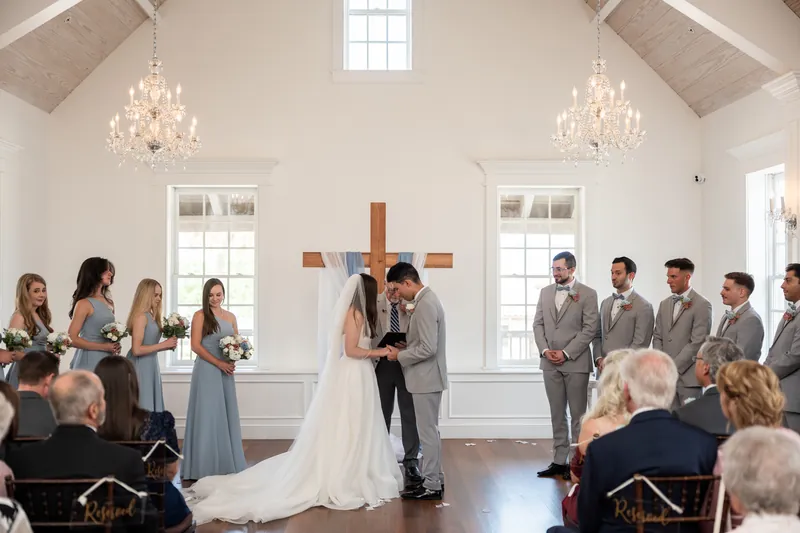 Nathan and Sarah stand before their officiant beneath crystal chandeliers as guests witness their ceremony in the elegant