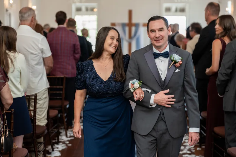 Nathan and Sarah smile while walking through their recessional as guests congratulate them from the pews around them.