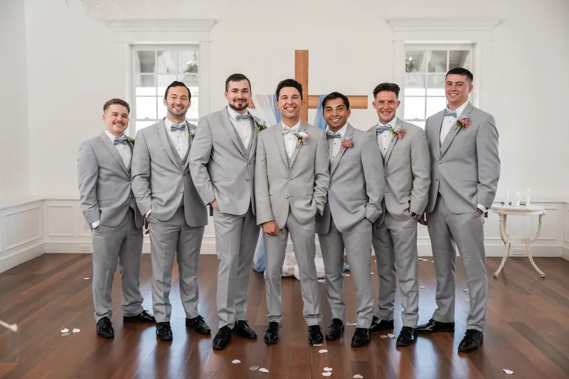 Nathan and seven groomsmen stand shoulder-to-shoulder in coordinating gray suits, smiling at the camera inside The White