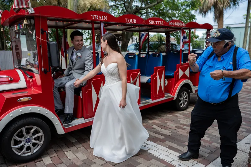 Nathan helps Sarah step onto a red trolley tour car in downtown St. Augustine as an operator watches.