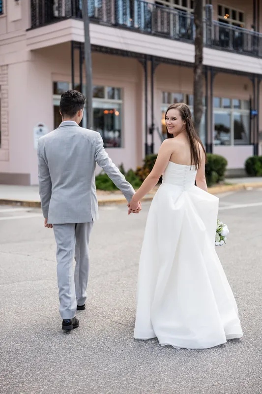 Sarah and Nathan walk hand-in-hand down a tree-lined street in Downtown St. Augustine, with storefronts visible behind them.