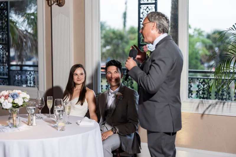 A male guest speaks at a microphone while Nathan and Sarah listen from their table at The White Room.