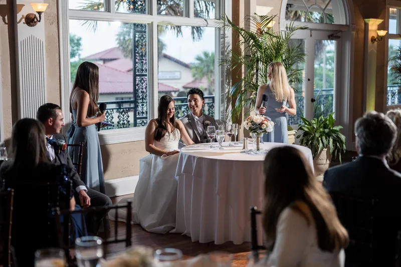 Sarah and Nathan sit at a sweetheart table as a speaker addresses guests during their reception.