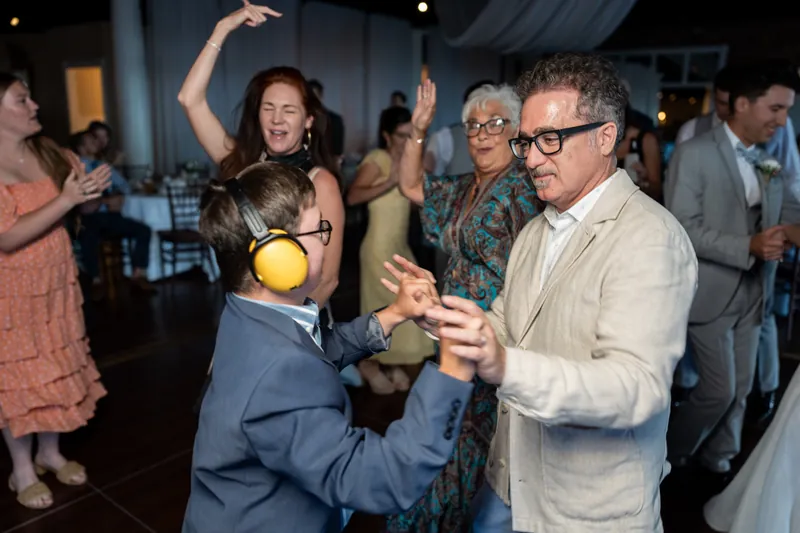 A child in a navy suit dances with a man in a cream shirt on the dance floor surrounded by guests.