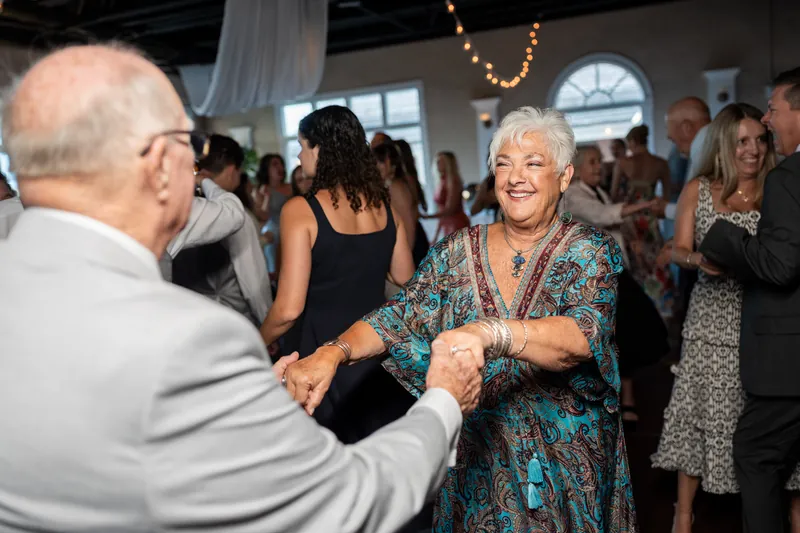 Woman in teal patterned dress clasps hands with a guest during reception dancing at The White Room.