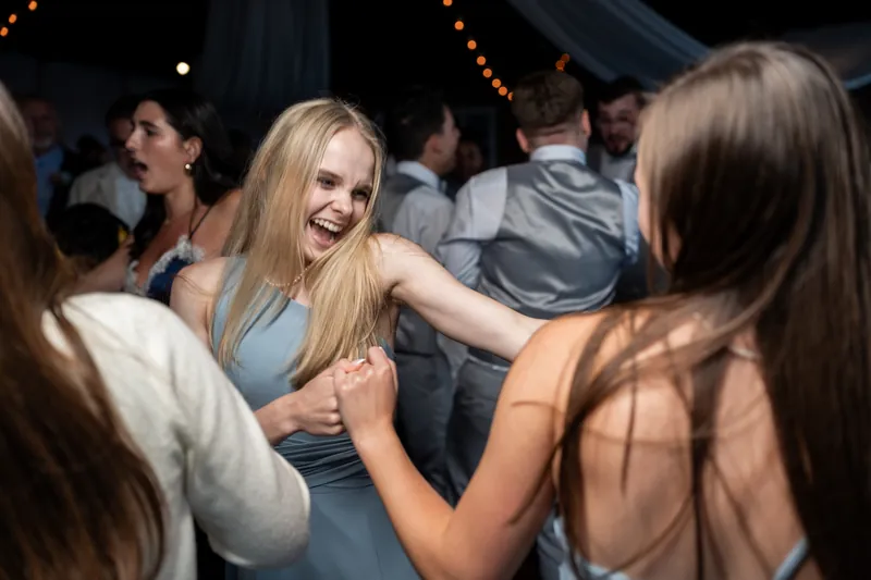 Guest in light blue dress laughs and dances with friends under string lights at the reception.