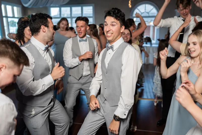 Nathan dances with groomsmen in gray vests and white shirts as guests surround them on the dance floor.