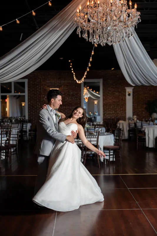 Sarah and Nathan dance under draped fabric and a crystal chandelier at The White Room, St. Augustine, as guests watch