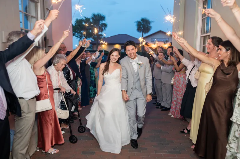 Guests form a line with raised arms as Sarah and Nathan walk between them at dusk on The White Room's exterior terrace.