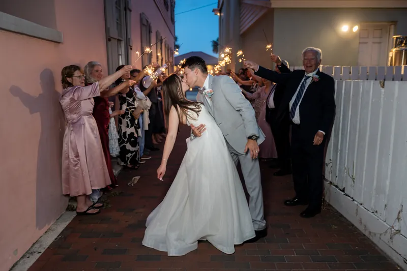 Nathan and Sarah walk hand-in-hand through a sparkler tunnel lined by guests on a brick courtyard at The White Room.