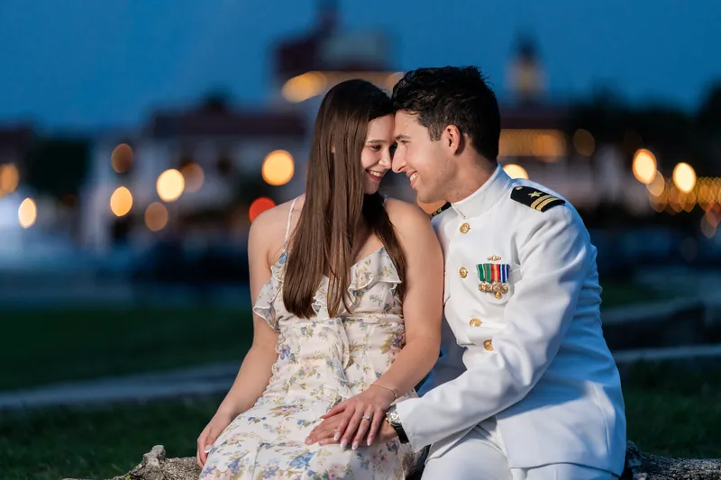 Two people sit close together at twilight with the illuminated Castillo de San Marcos glowing behind them.