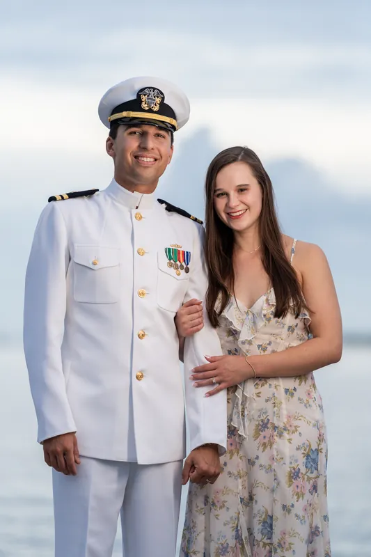 Nathan in naval whites and Sarah Katherine in a patterned dress smile together with the fortress and cloudy sky behind them at Castillo de San Marcos.