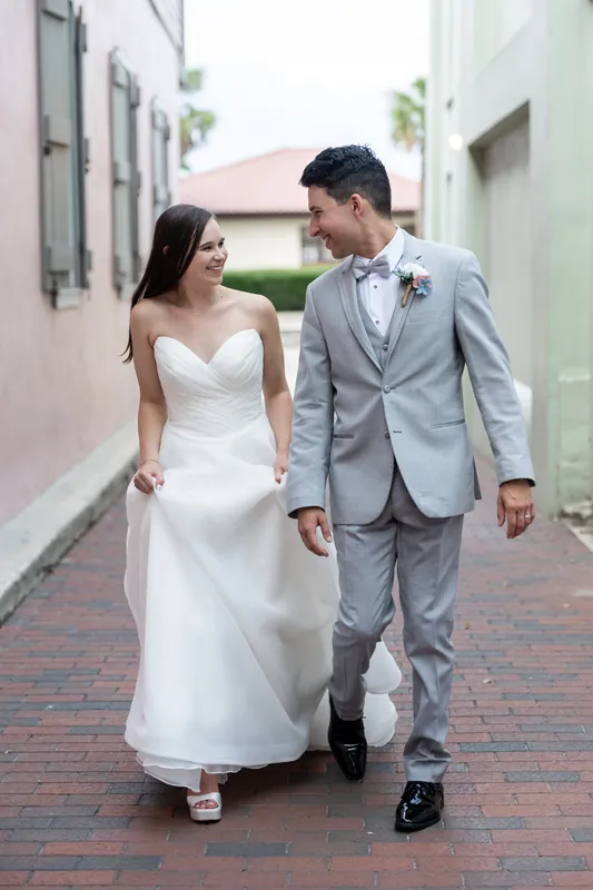 Two people walk hand-in-hand down a brick pathway bordered by colonial buildings at The White Room.