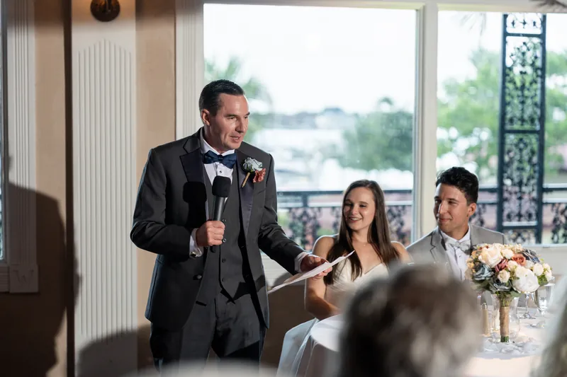 A person in a dark suit speaks at a table while two seated guests listen during the reception at The White Room, St. Augustine.