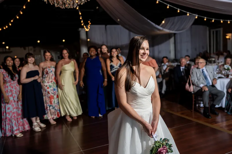 Sarah Katherine walks across the dance floor in her white gown, holding her bouquet as guests look on.