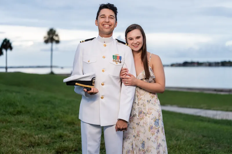 Sarah Katherine and Nathan hold a sword between them on the grounds at Castillo de San Marcos, with palm trees and water visible across the landscape.