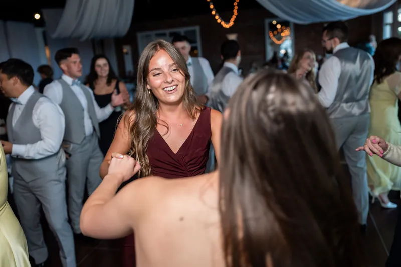 A woman in a burgundy velvet top smiles while dancing at The White Room, surrounded by guests in formal attire.