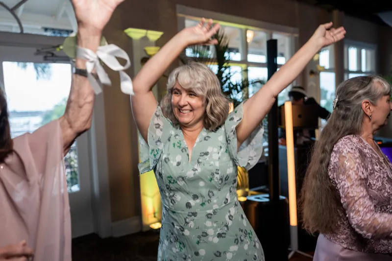 A woman in a sage floral dress celebrates with raised arms on the dance floor at The White Room.