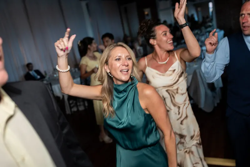 Guests celebrate on the dance floor at The White Room, with a woman in a teal sash dancing energetically alongside others in formal wear.