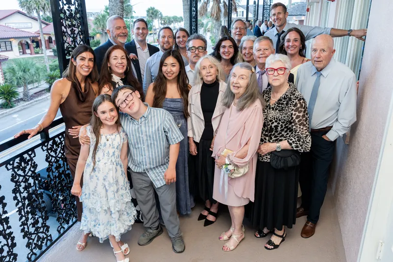 Fifteen guests gather for a formal group portrait on a terrace with palm trees and waterfront views at The White Room, St. Augustine.