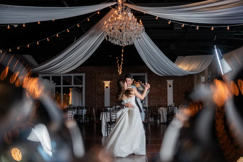 A couple dances under draped white silk and a crystal chandelier as guests celebrate around them at The White Room, St. Augustine.