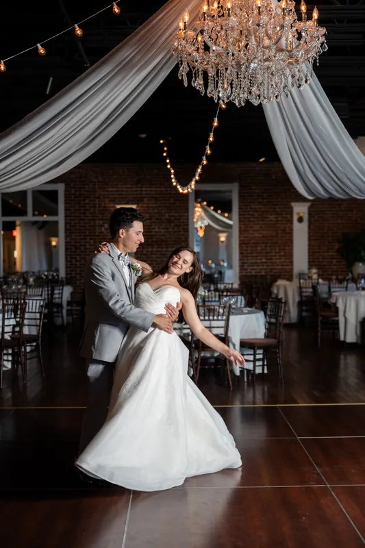 Nathan twirls his partner in a white gown across the dance floor beneath ornate draping and a chandelier at The White Room, St. Augustine.