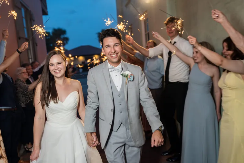 Two people hold hands and smile while walking through a sparkler tunnel held by wedding guests at The White Room, St. Augustine.