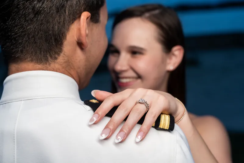 A close detail of two hands, one in a white sleeve, the other displaying a diamond ring as they embrace with evening light in the background.