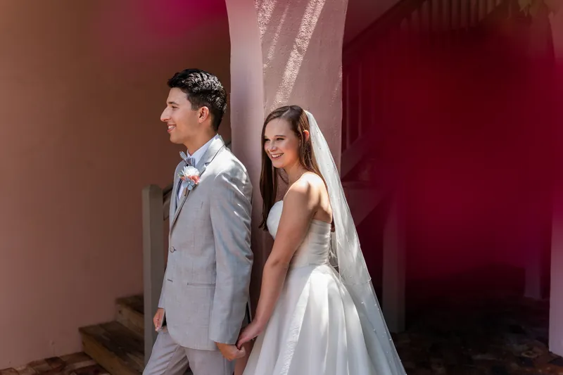 Two people in wedding attire stand in profile against a deep burgundy wall at The White Room.