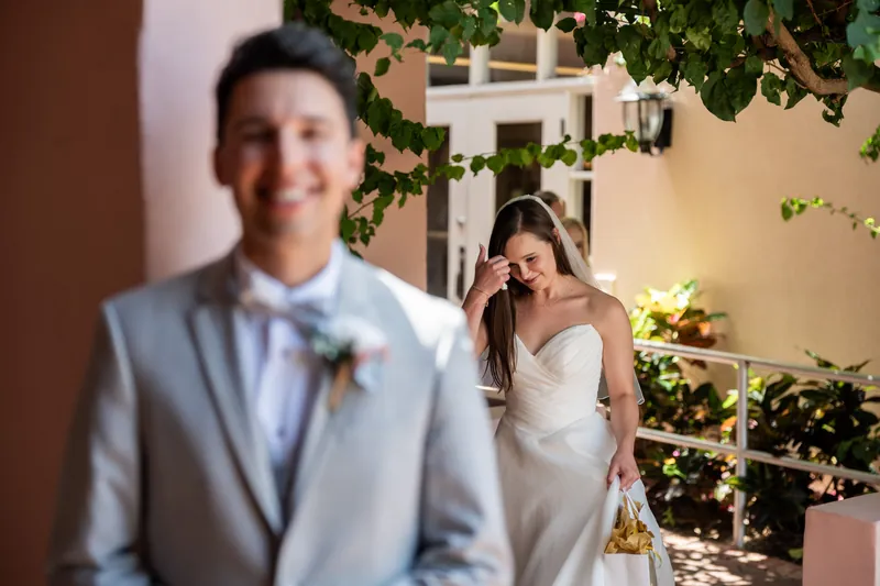 A person in a light blue suit stands before someone in a white strapless gown framed by ivy in a courtyard.