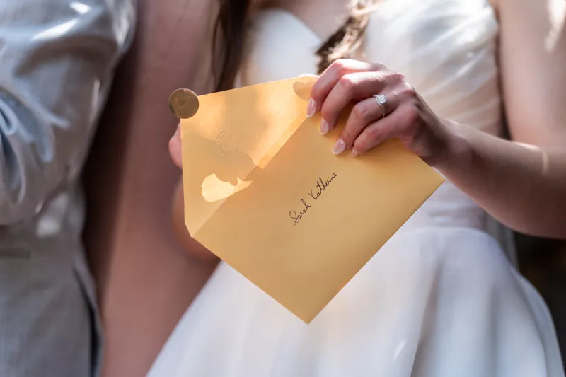 Hands hold an open gold envelope with "Sarah" written on it during the gift-opening moment.