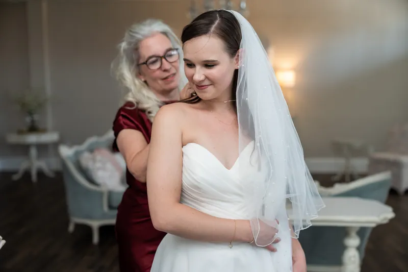 An older woman in burgundy embraces a person wearing a white gown and veil at The White Room.