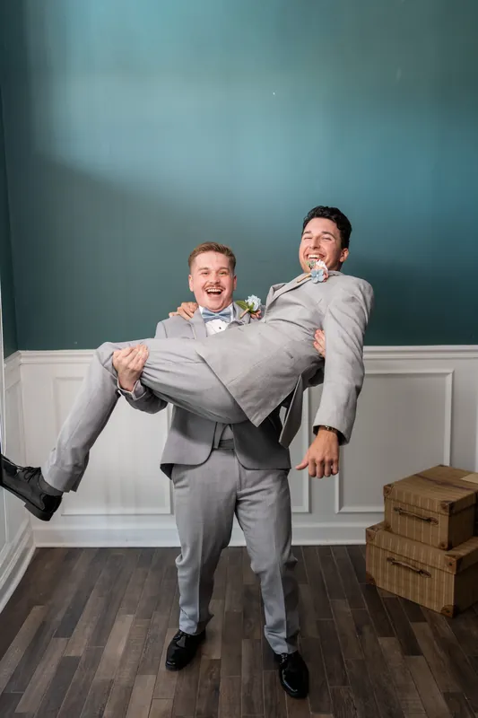 One person in a gray suit lifts another in gray suit at the waist inside The White Room's contemporary space.