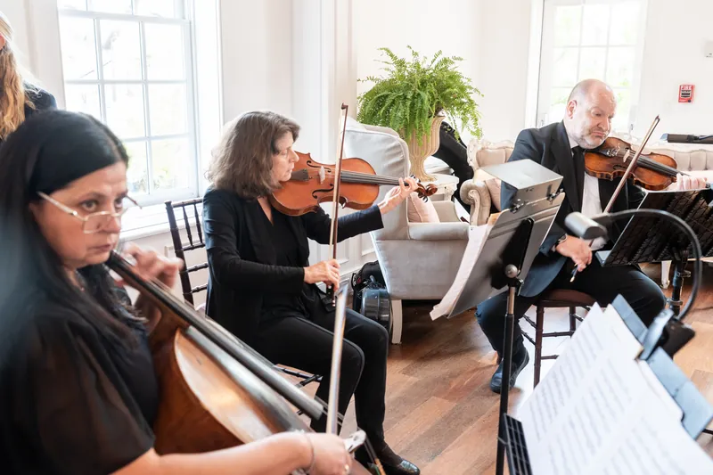 String quartet performs in period attire, reading sheet music during a ceremony at The White Room's brightly lit hall.