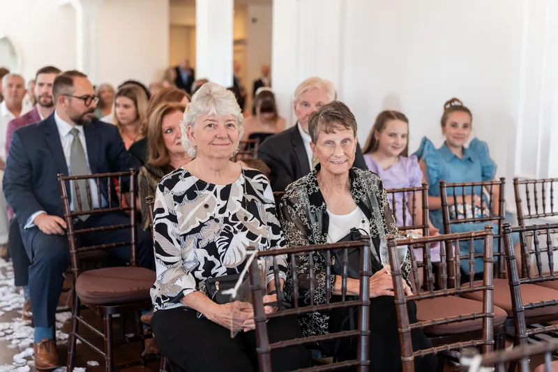 Guests seated on wooden chairs face forward during a ceremony in The White Room's bright, high-ceilinged chapel space.
