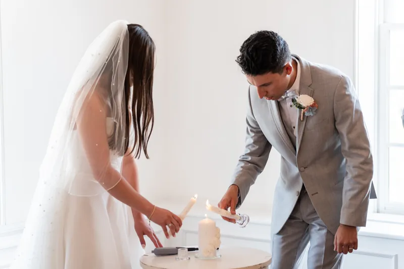 A couple in white gown and gray suit places a hand on a white box during a unity ritual at The White Room, St. Augustine.