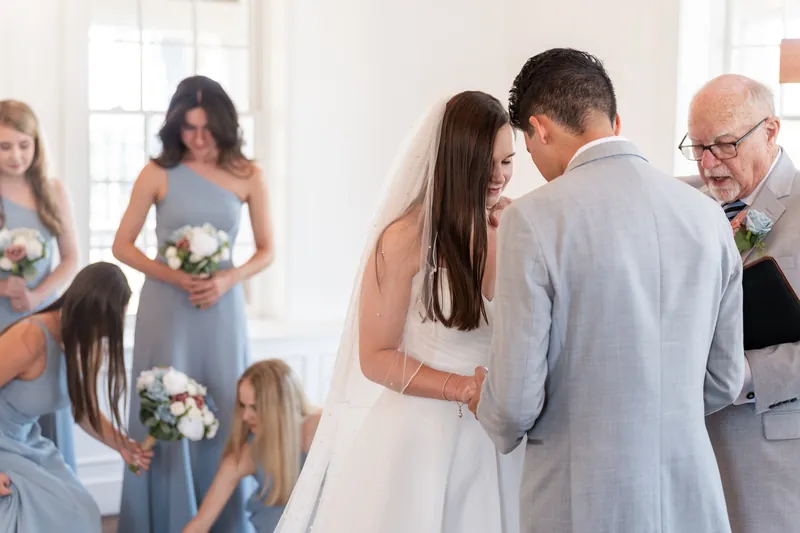 A person in a white gown smiles while embracing a partner in gray as wedding party members look on at The White Room, St. Augustine.