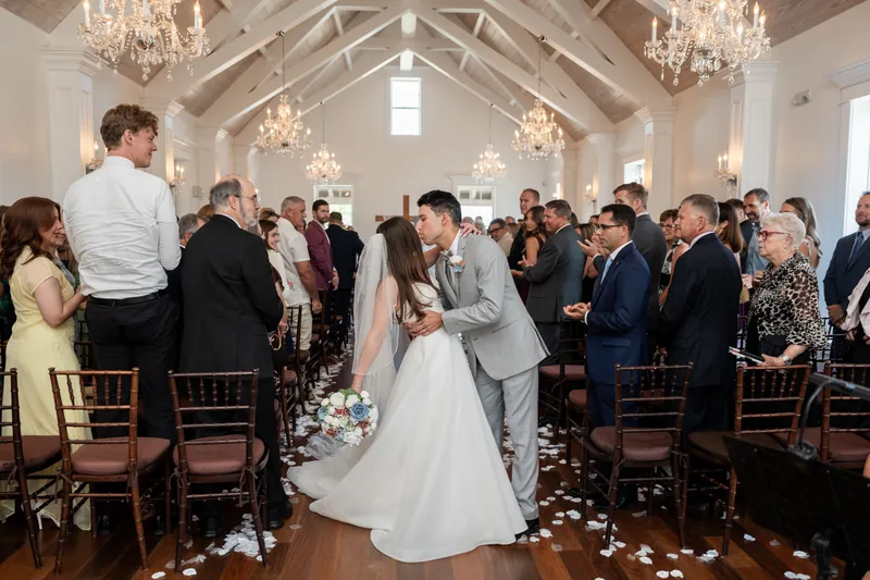 The couple walks through their cheering wedding party down a petal-strewn aisle lined with brown chiavari chairs.
