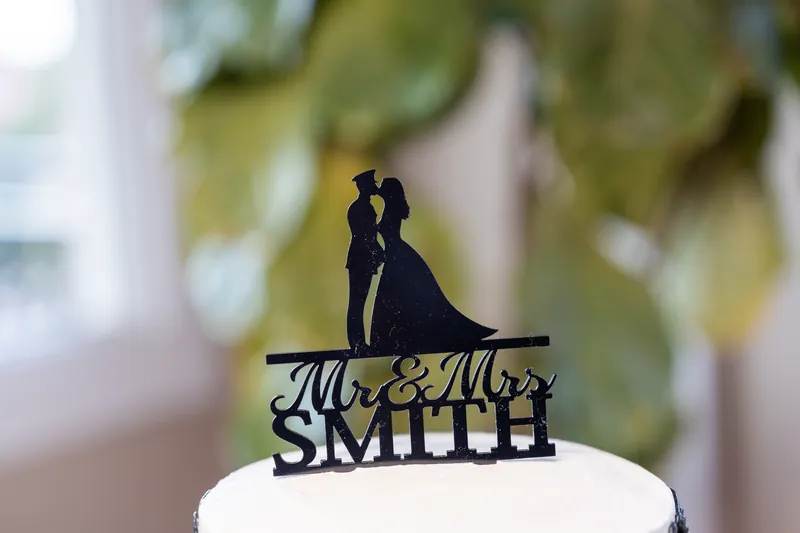 Black silhouette cake topper reading "Mr & Mrs SMITH" sits atop white frosting.