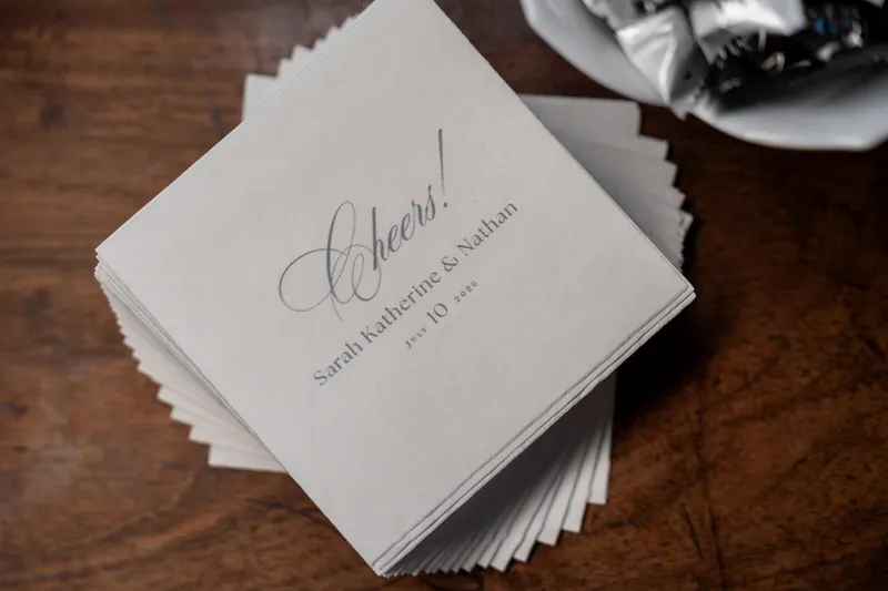 Stack of white ceremony programs with calligraphy sits on a wood table beside a place setting.